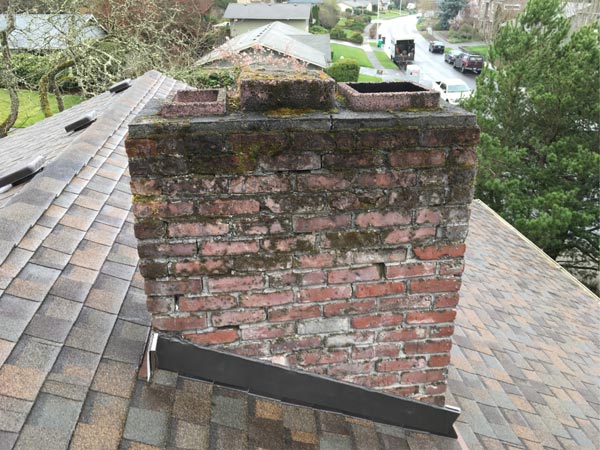 A weathered brick chimney on a shingled roof before repair A weathered brick chimney on a shingled roof before repair
